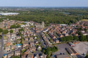 Aerial Image showing the historic Church of St James with St Thomas surrounded by modern residential streets in Poolstock, with expansive Westwood Woods stretching across the background in Wigan.